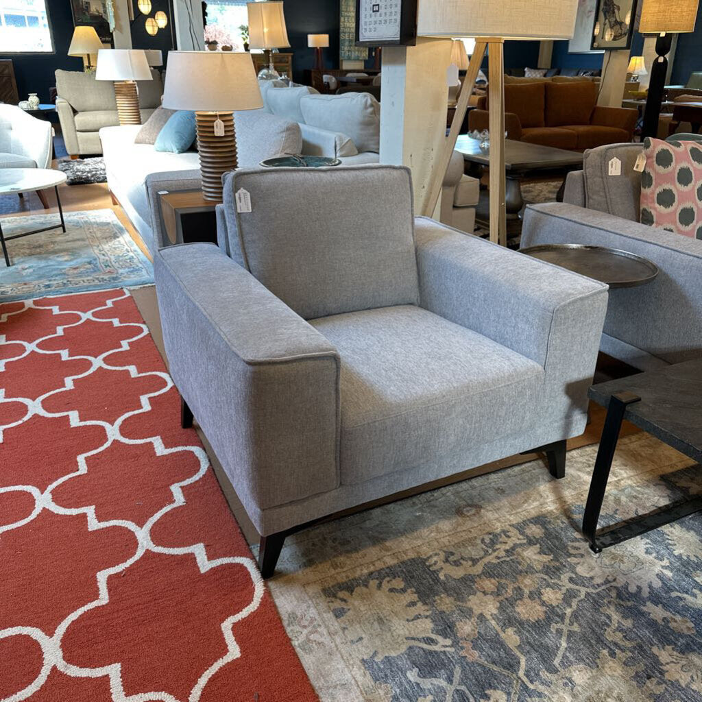 Gray armchair in a showroom with various furniture and decor items.