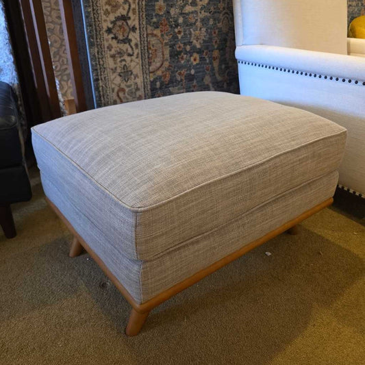 Beige ottoman with wooden legs in a room setting