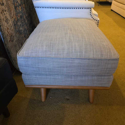 Gray upholstered footstool with wooden legs in a room setting