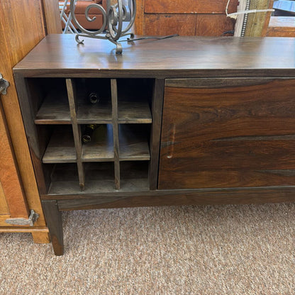 Wooden sideboard with wine rack and closed door on a carpeted floor.