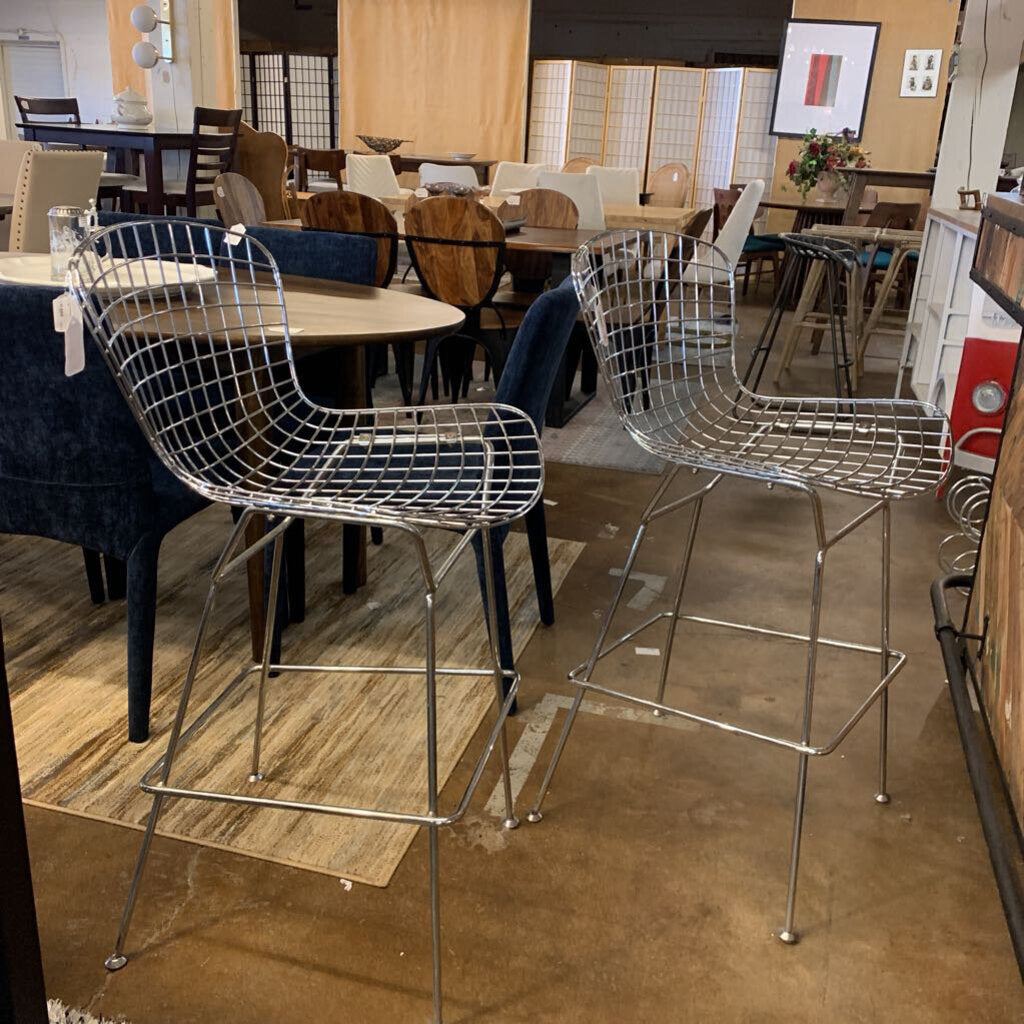 Metallic bar stools in a showroom setting with tables and chairs in the background.