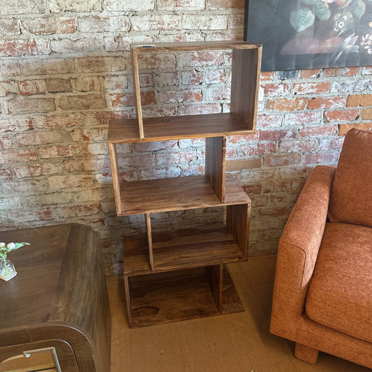 Wooden bookshelf against a brick wall with a brown sofa and table in the foreground.