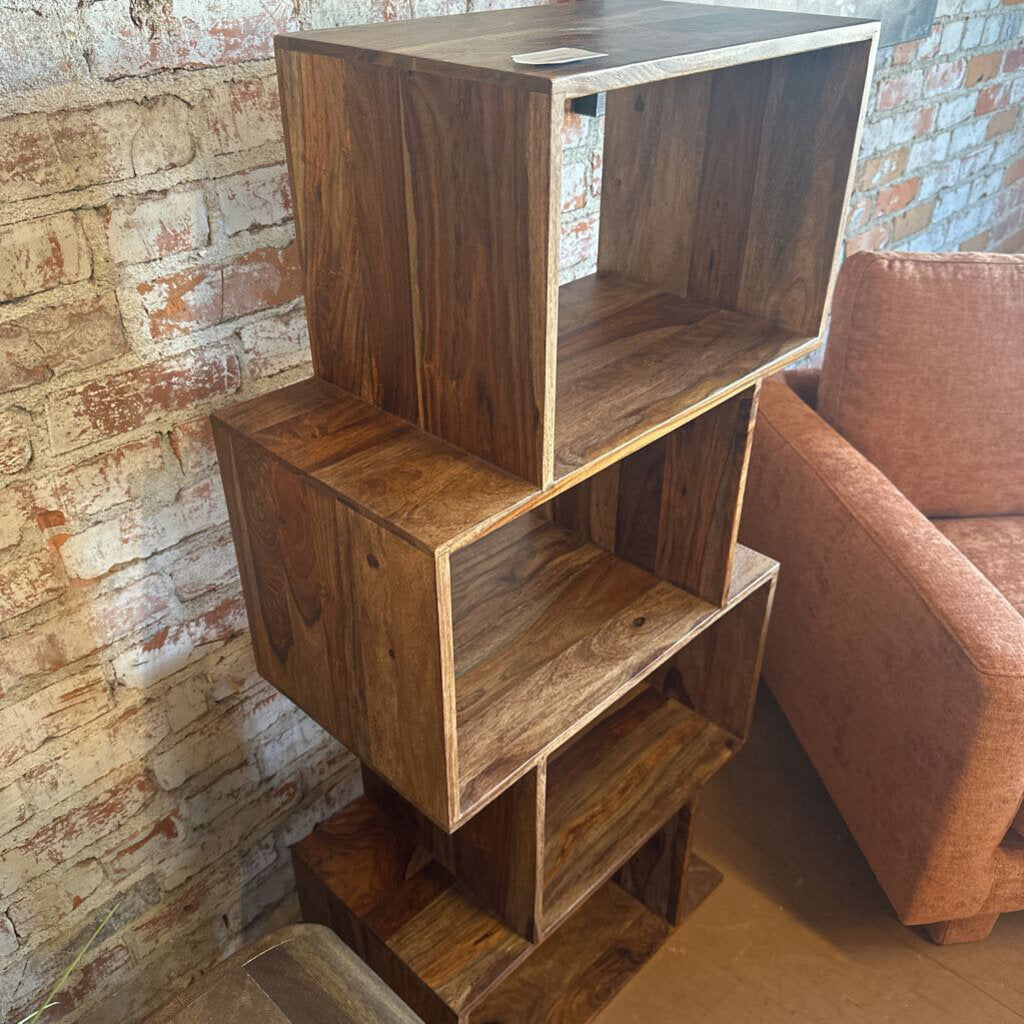 Wooden bookshelf against a brick wall with a brown armchair.