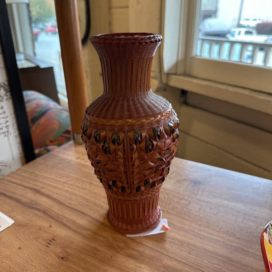 Brown woven vase on a wooden surface with a blurred background