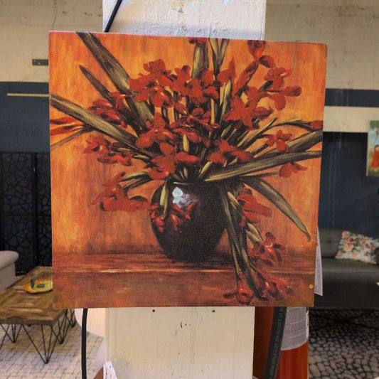 Painting of red flowers in a vase on an easel in a room setting.