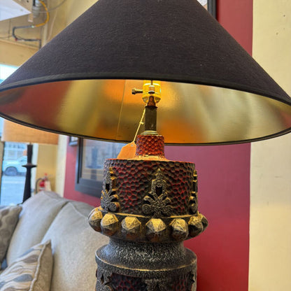Decorative lamp with a black shade and textured base in a room setting.