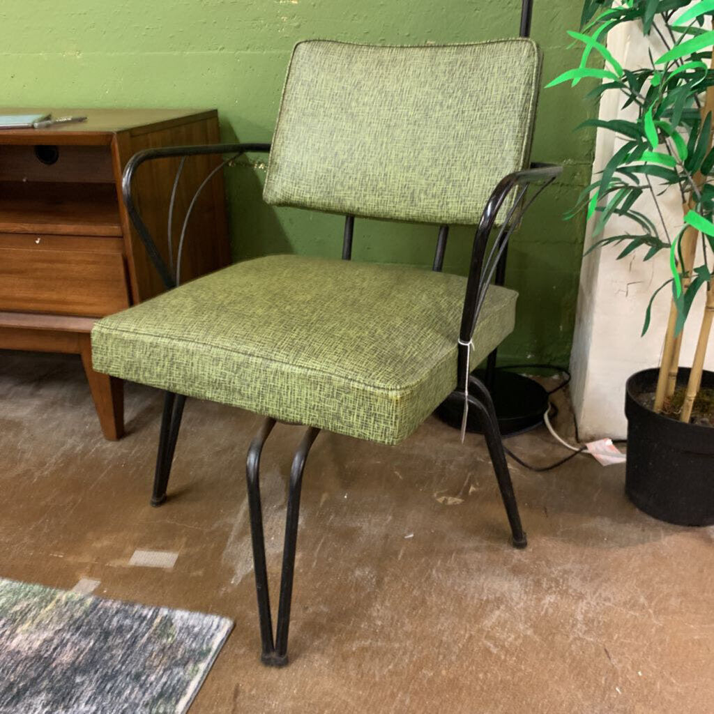 Green upholstered chair with metal frame in a room with a desk and plant.