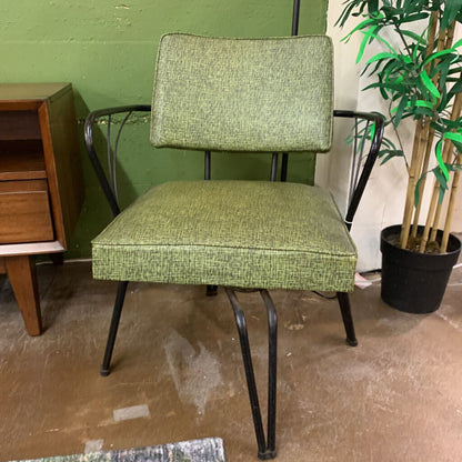 Green upholstered chair with metal legs in a room with a green wall and a plant.