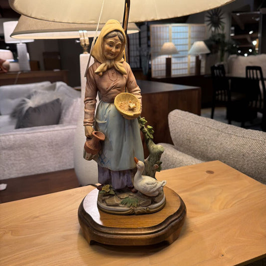 Decorative figurine of a woman with a goose on a wooden base in a living room setting.