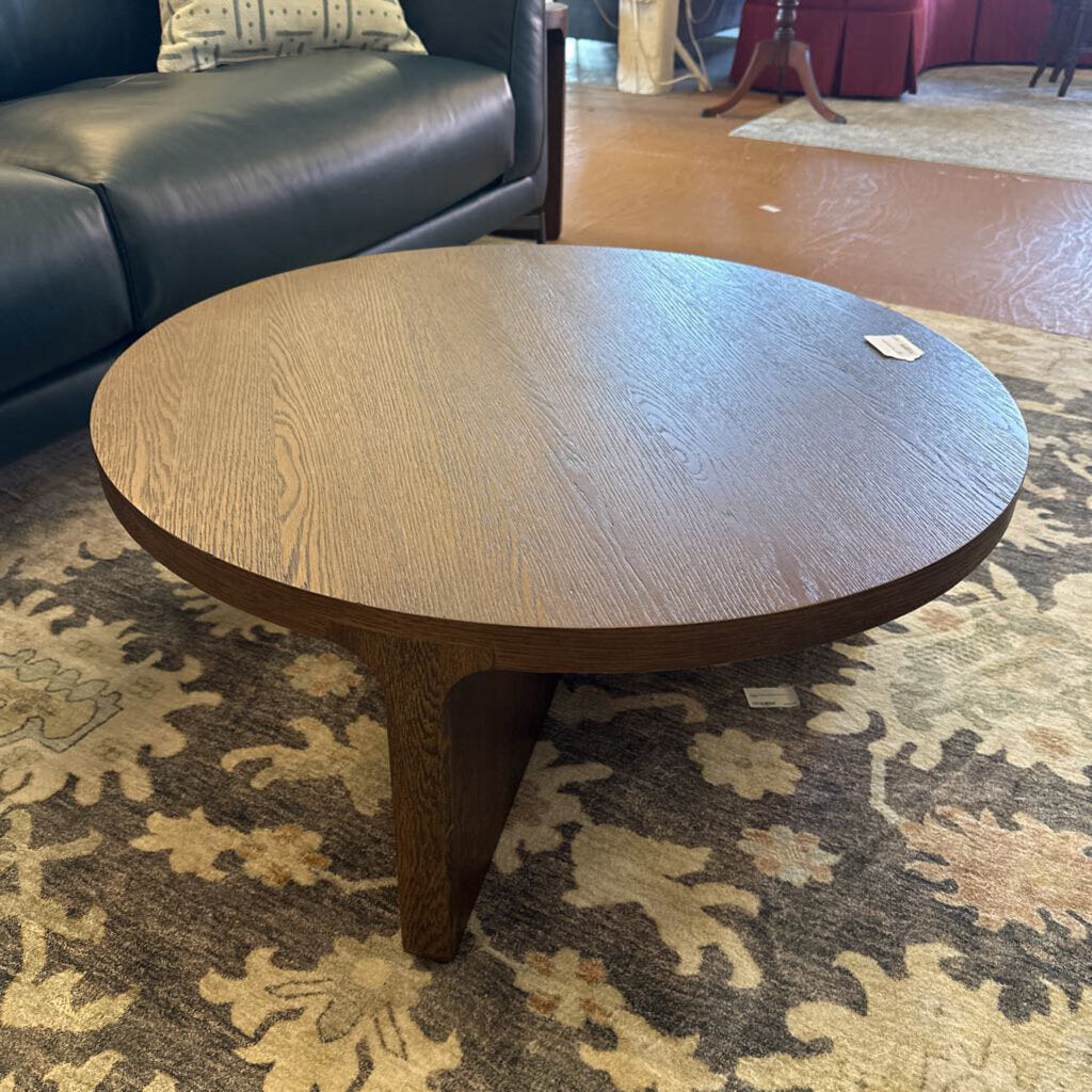 Round wooden coffee table on a patterned rug with a dark sofa in the background