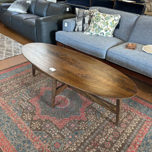 Wooden coffee table in front of a gray sofa with patterned cushions on a decorative rug.