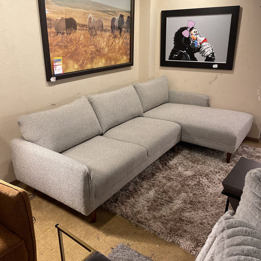 Gray sectional sofa in a living room with framed pictures on the wall.