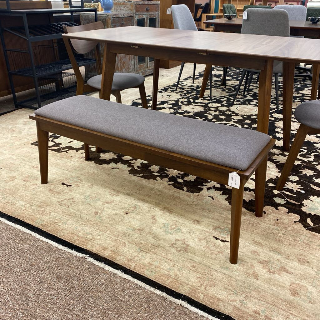 Wooden bench with gray cushion on a patterned rug in a store setting
