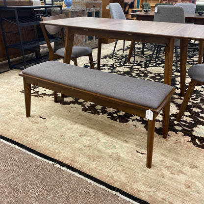 Wooden bench with gray cushion on a patterned rug in a store setting
