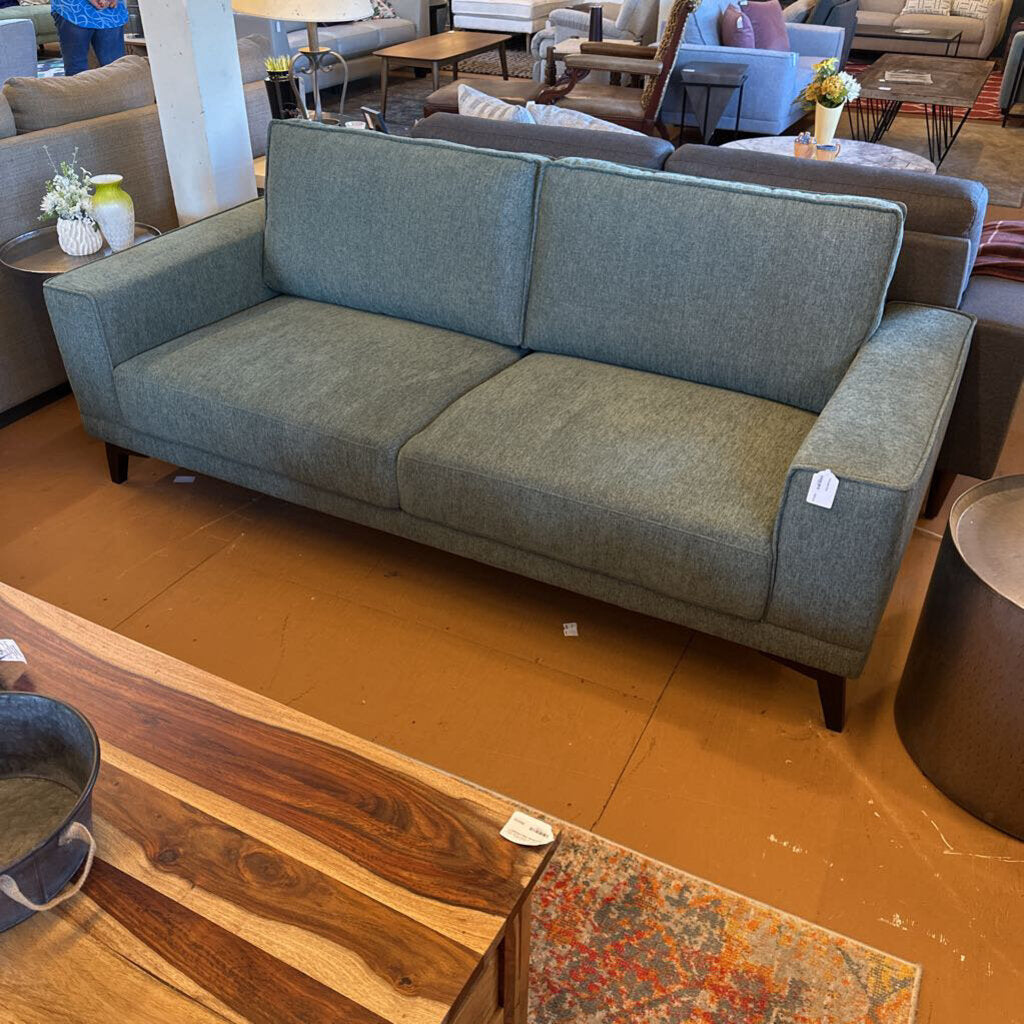 Gray sofa in a showroom with wooden floor and furniture in the background