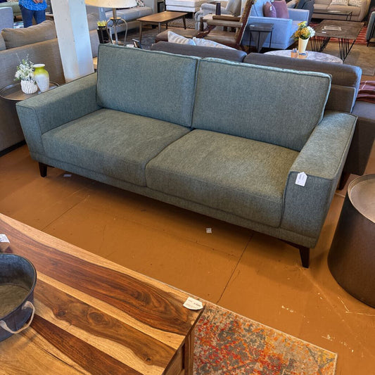 Gray sofa in a showroom with wooden floor and furniture in the background