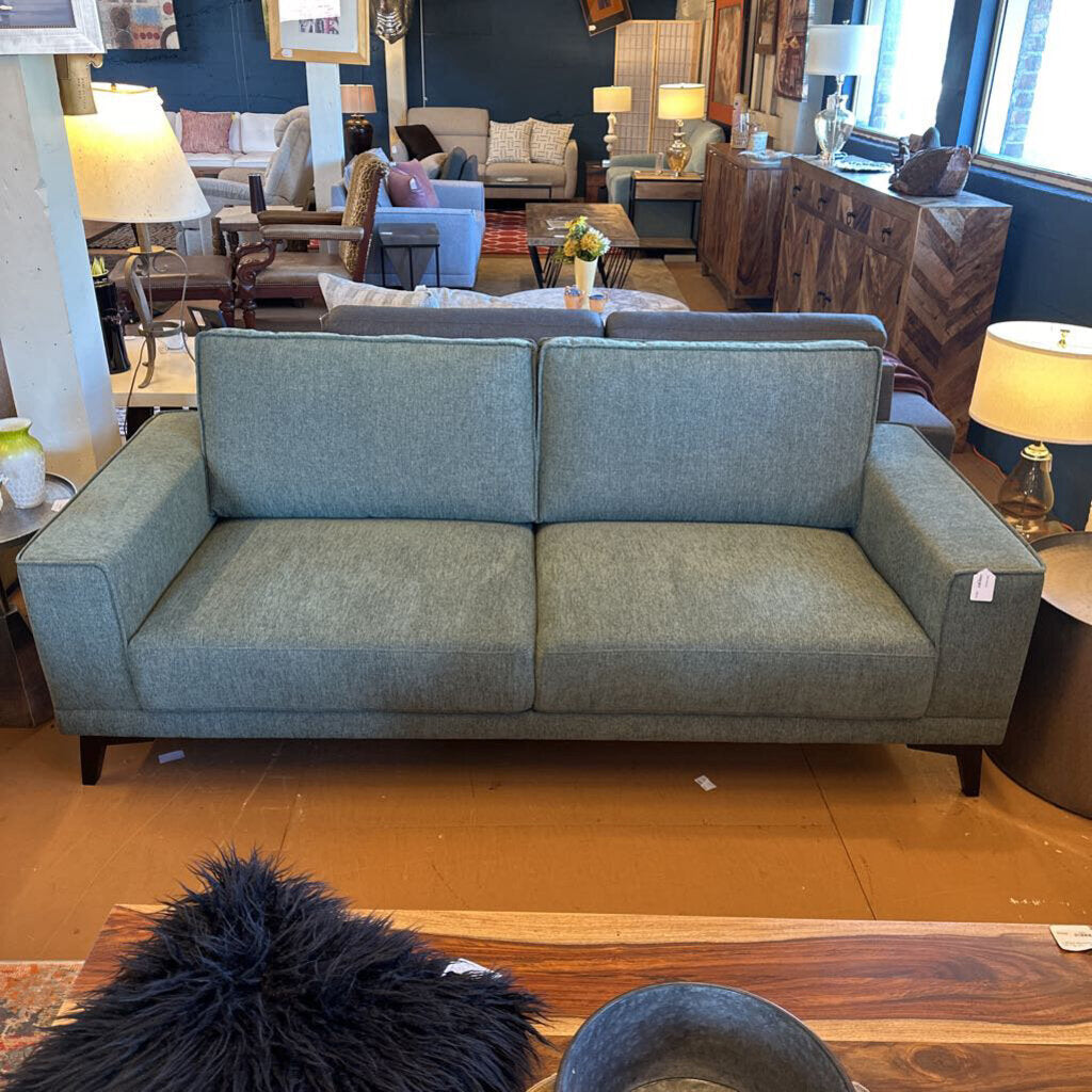 Green sofa in a showroom with various furniture and decor items.