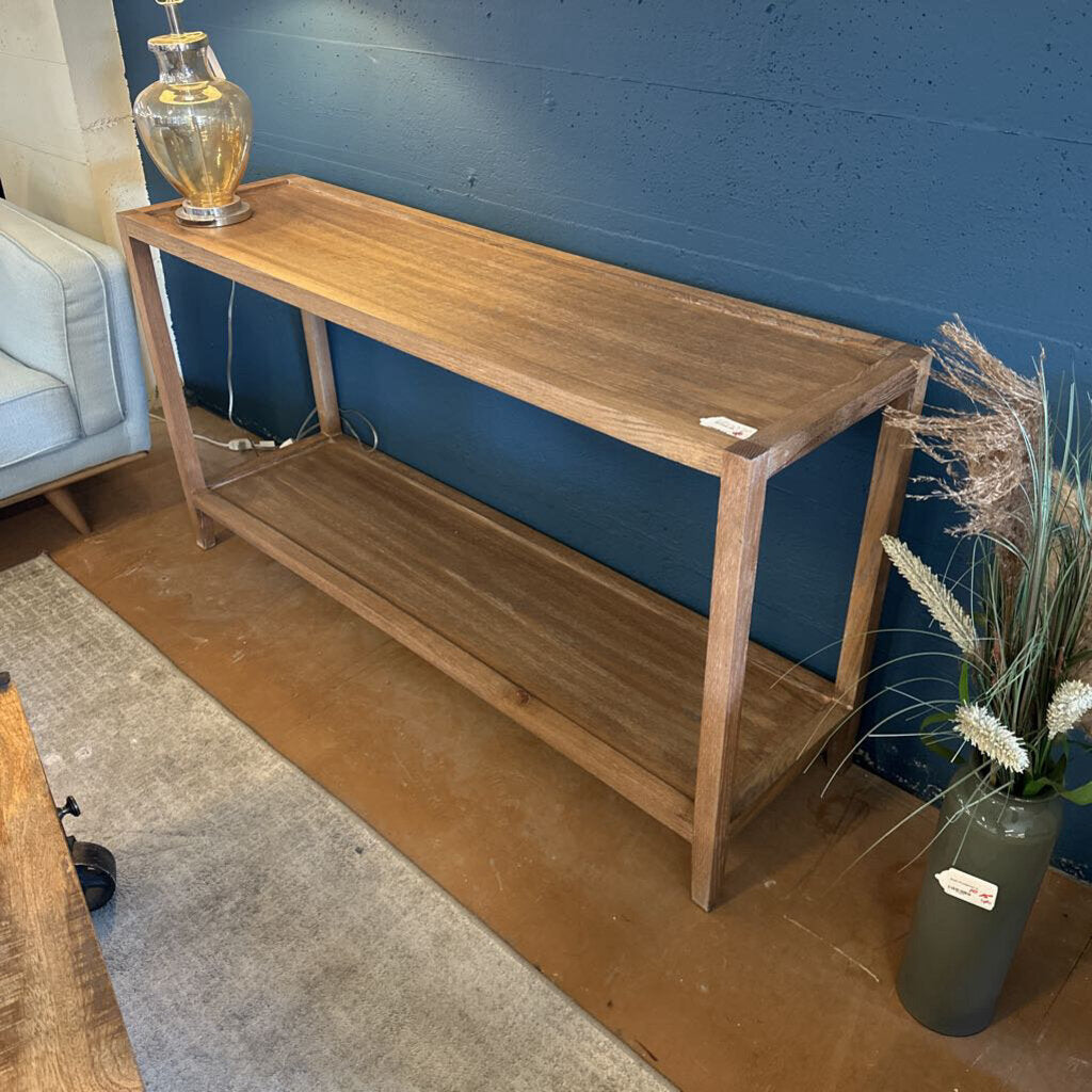 Wooden console table against a blue wall with a vase of flowers on a wooden floor.