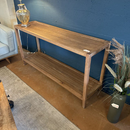 Wooden console table against a blue wall with a vase of flowers on a wooden floor.