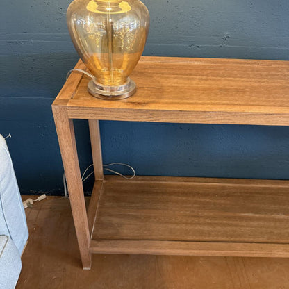 Wooden console table with a glass lamp against a blue wall
