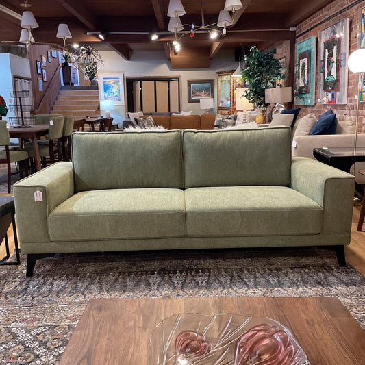 Green sofa in a furniture store with a wooden floor and various decor items.