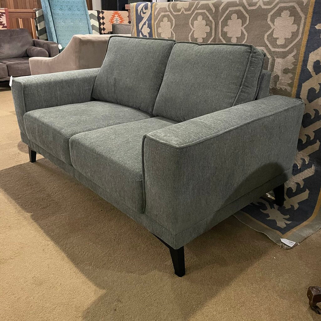 Gray sofa in a store setting with patterned rug in the background