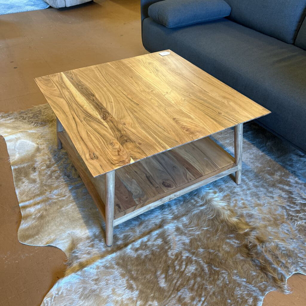 Wooden coffee table on a textured rug with a sofa in the background