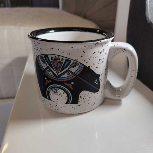 White mug with black speckles and a black bear design on a white surface.