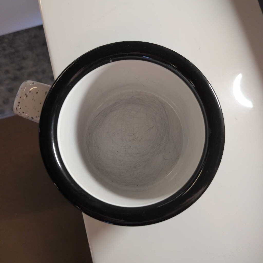 Close-up of a black coffee filter with a white mug inside on a white surface.