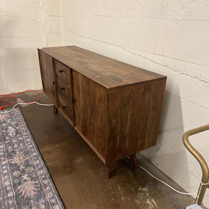 Wooden sideboard against a textured wall with a rug and chair in the foreground.