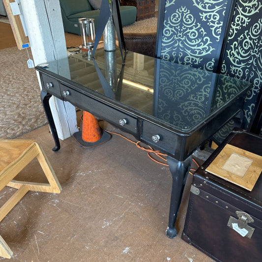 Black glass-top table with ornate chair in a room setting