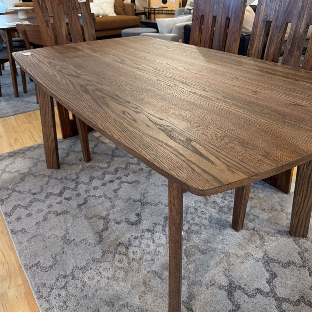 Wooden dining table on a patterned rug with chairs in the background