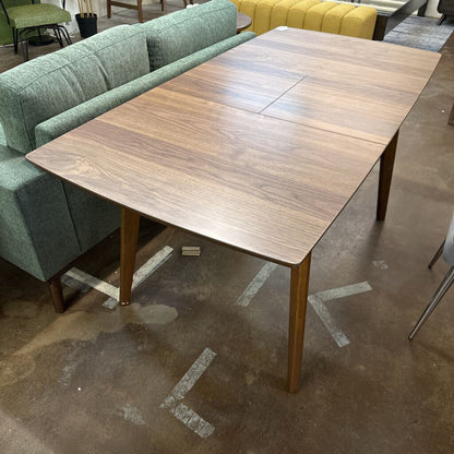 Wooden dining table in a room with green upholstered chairs and a gray floor.