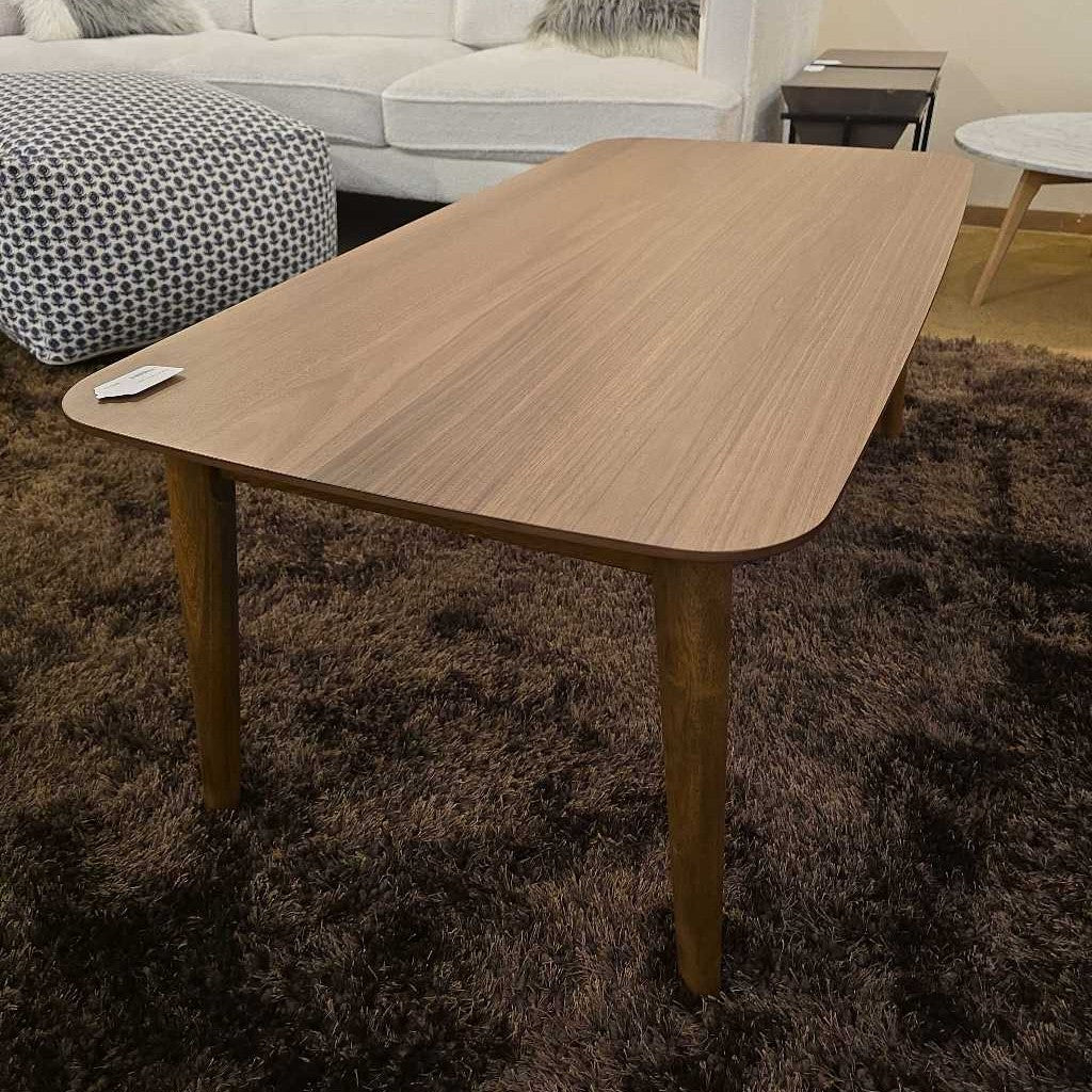 Wooden dining table in a living room setting with a brown rug and sofa.
