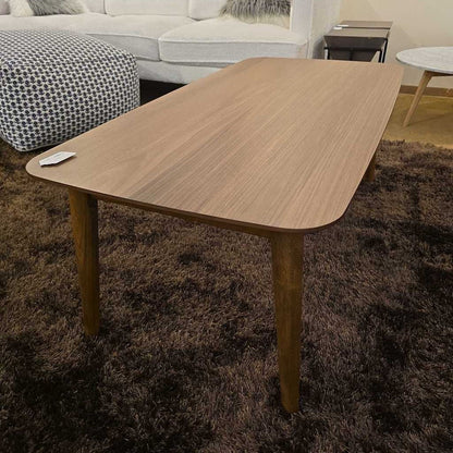 Wooden dining table in a living room setting with a brown rug and sofa.