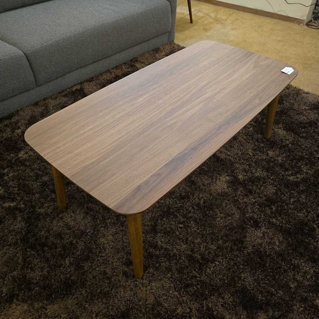 Wooden coffee table on a dark rug with a gray sofa in the background