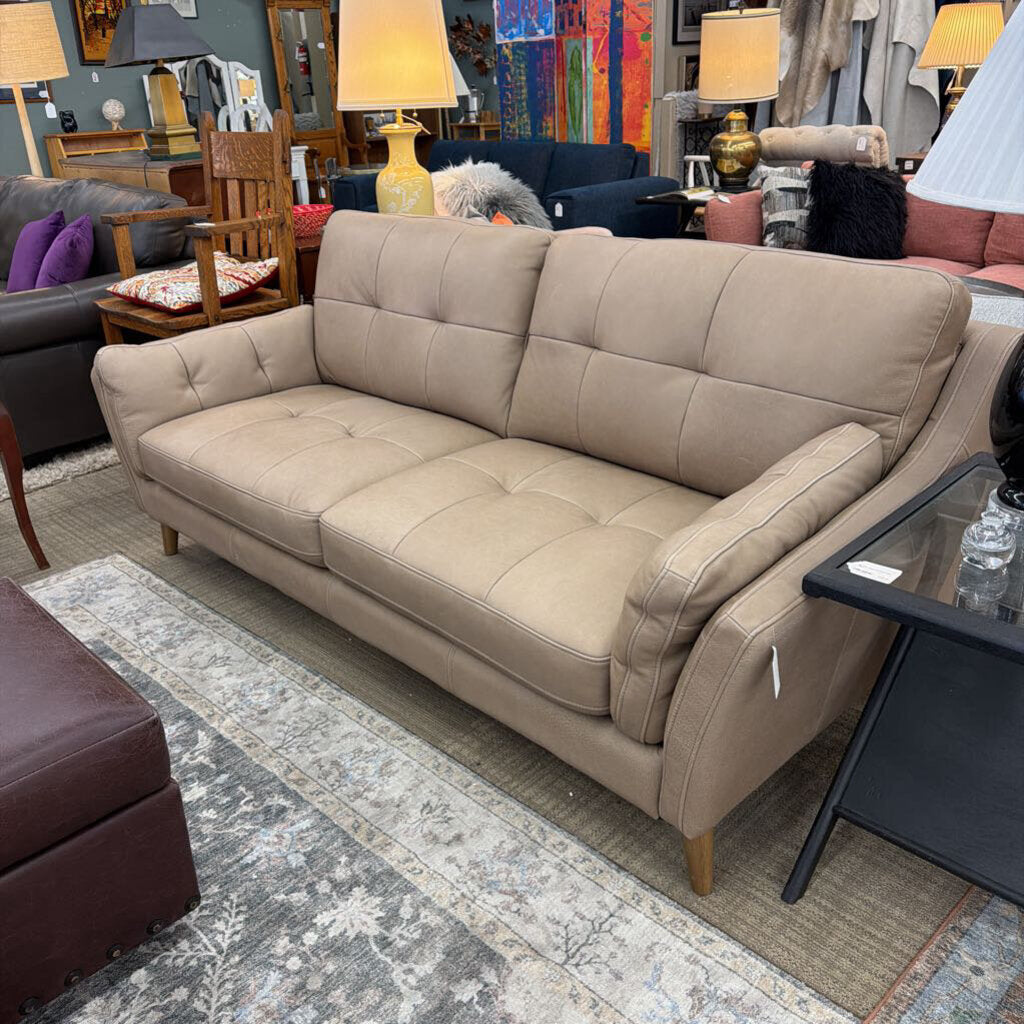 Beige sofa in a room with various furniture and decor items.