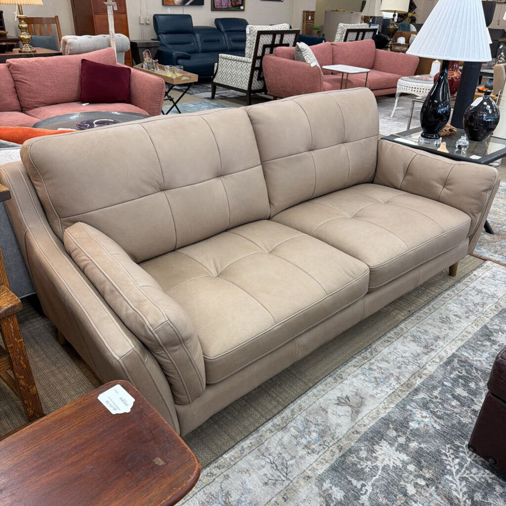 Beige sofa in a furniture store setting with other furniture items around.