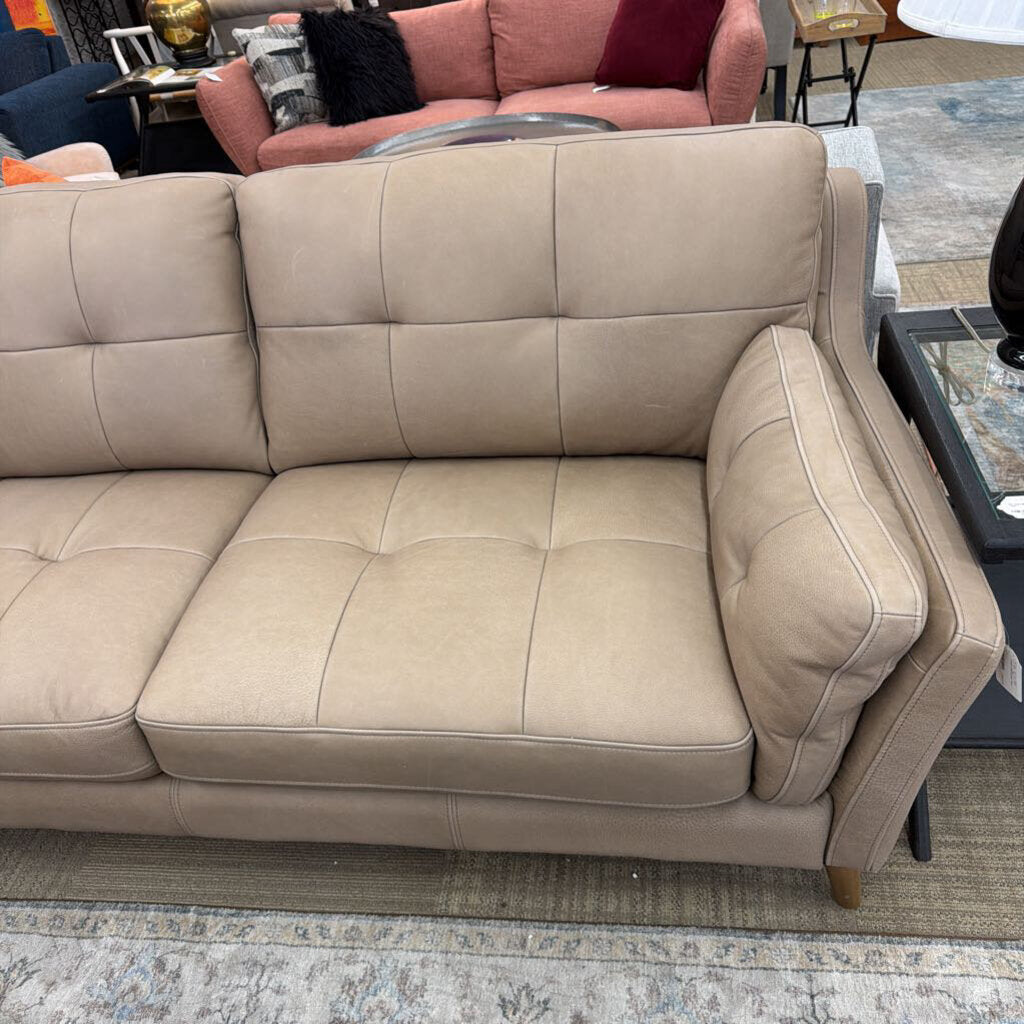 Beige sofa in a living room setting with a couch and chair in the background.