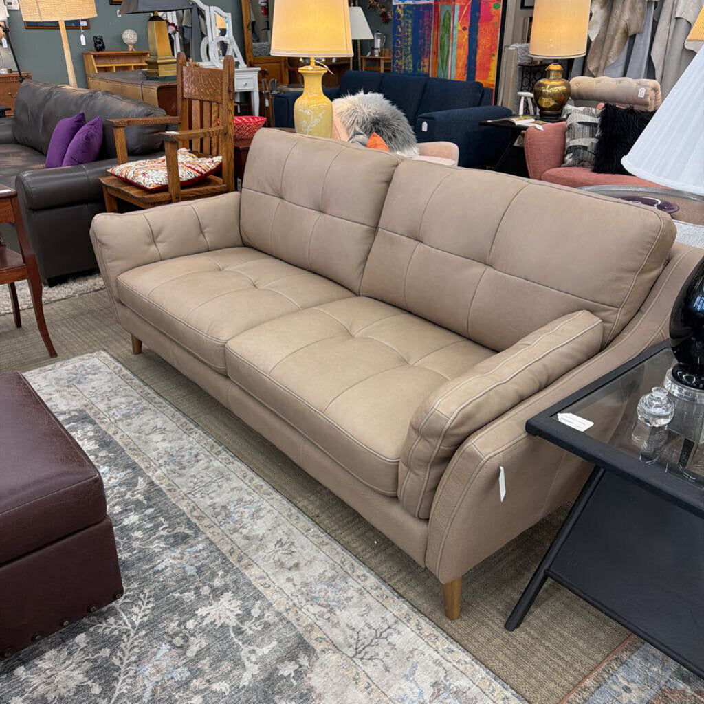 Beige sofa in a furniture store setting with various items in the background