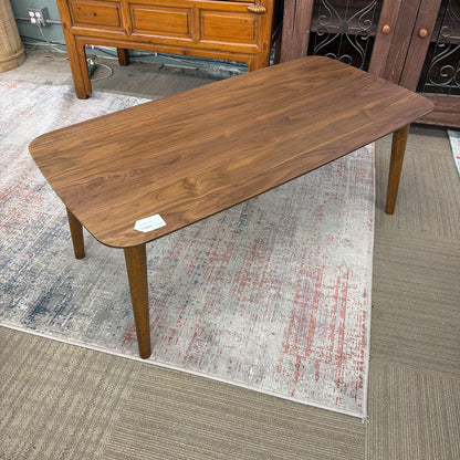 Wooden coffee table on a patterned rug with a wooden cabinet in the background.