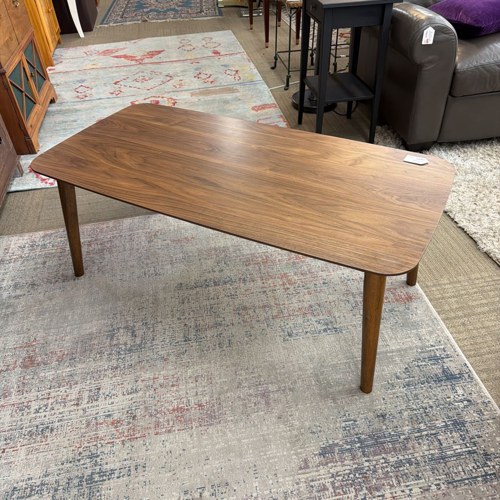 Wooden coffee table on a patterned rug in a room with furniture.