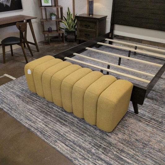 Yellow ottoman in front of a bed in a room with wooden furniture and decor.