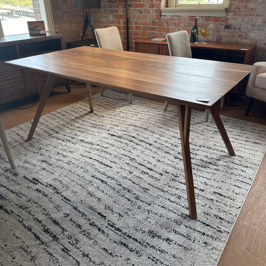 Wooden dining table in a room with a patterned rug and chairs.