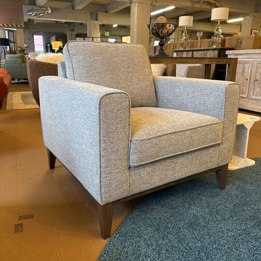 Gray armchair in a showroom setting with other furniture and decor items.