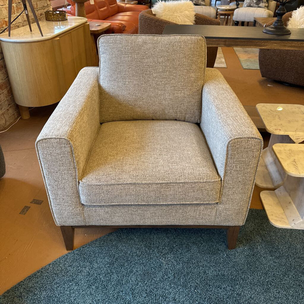 Gray armchair in a showroom setting with other furniture in the background