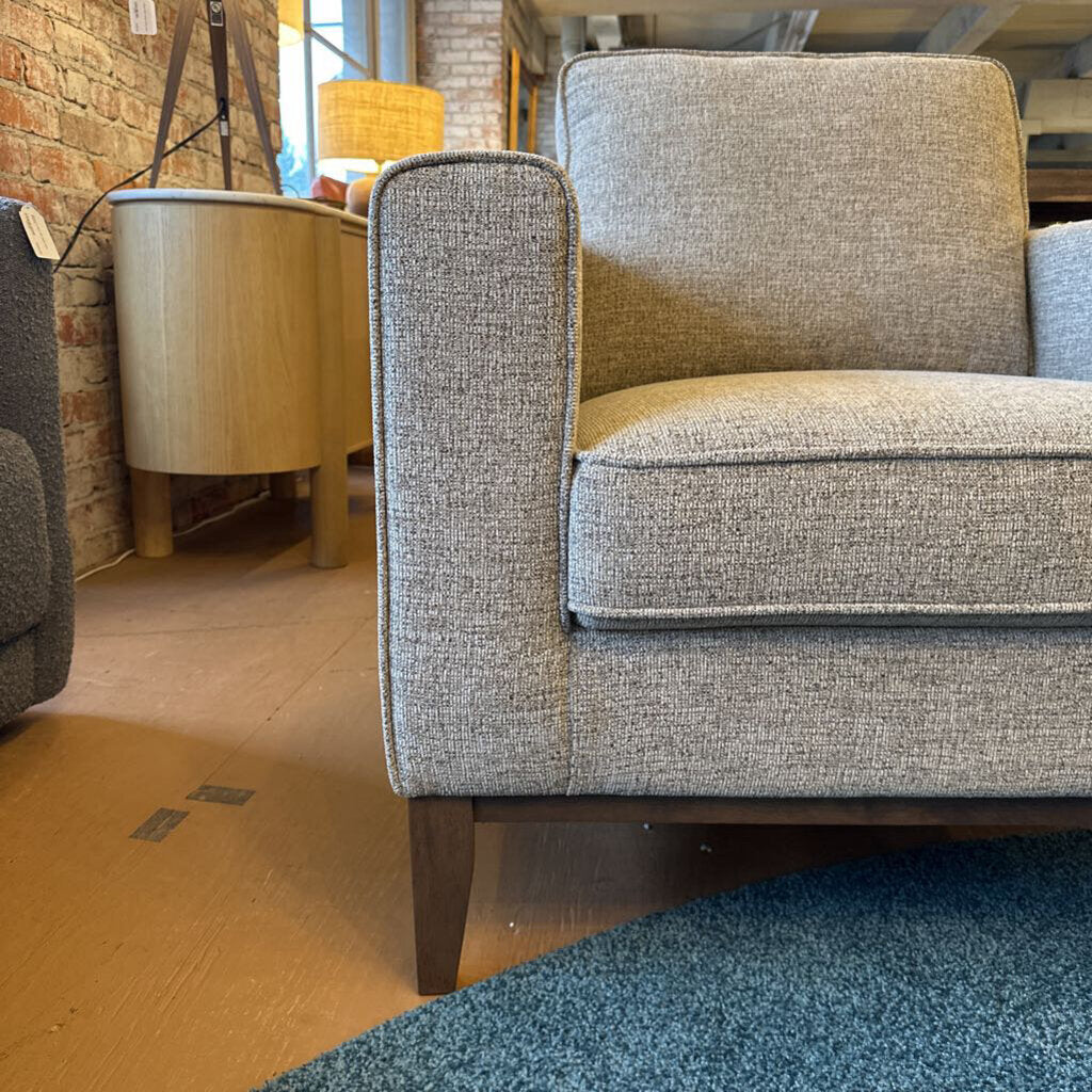Gray upholstered chair in a room with a brick wall and wooden floor.