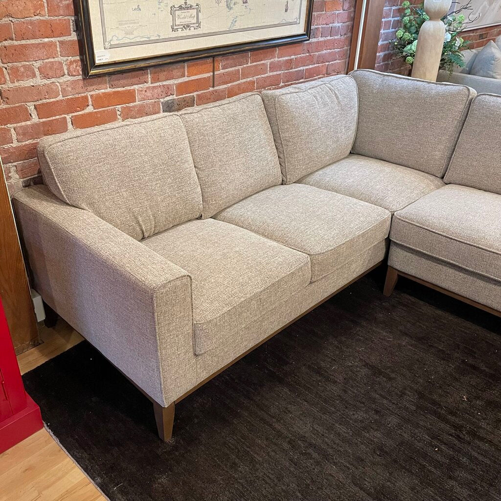 Beige sectional sofa in a room with brick walls and a plant.