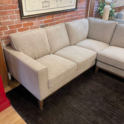 Beige sectional sofa in a room with brick walls and a plant.