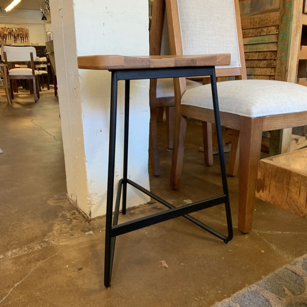 Tall black metal bar stool with a wooden seat in a room with chairs and tables.
